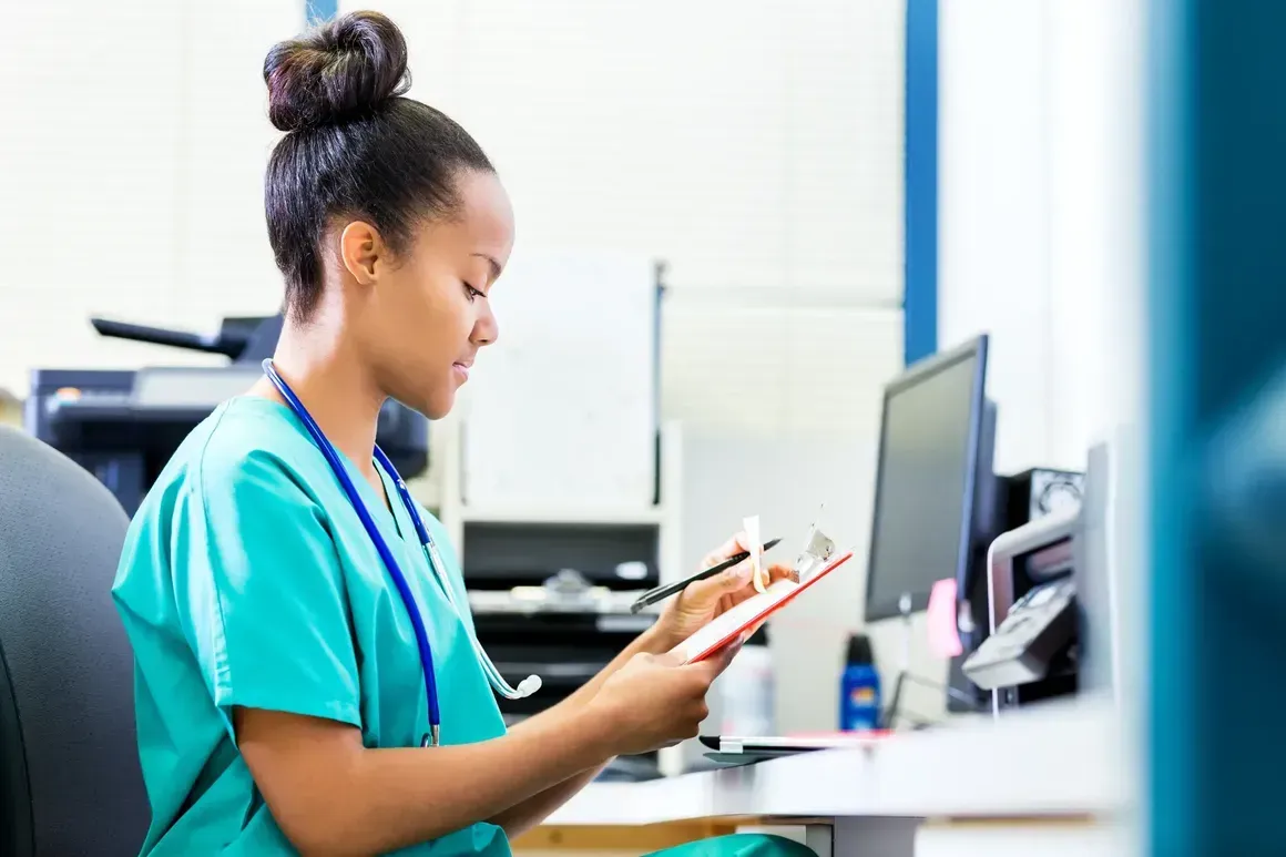 A nurse is sitting at a desk looking at a clipboard.