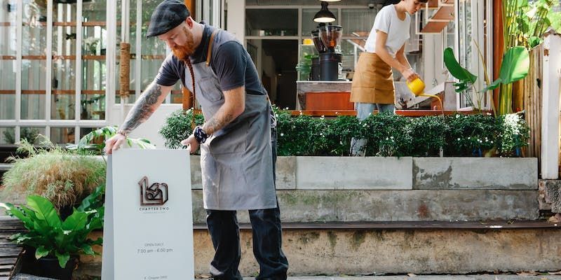 A man and a woman are watering plants outside of a restaurant.