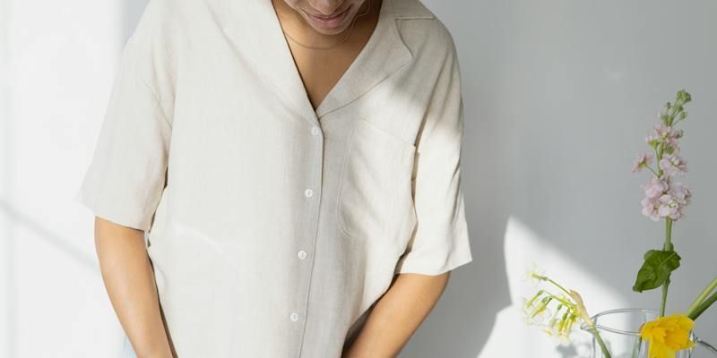 A woman in a white shirt is standing in front of a vase of flowers.