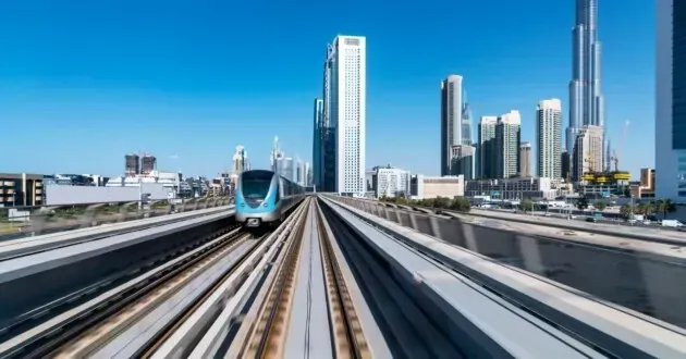 A train is going down train tracks in a city with skyscrapers in the background.