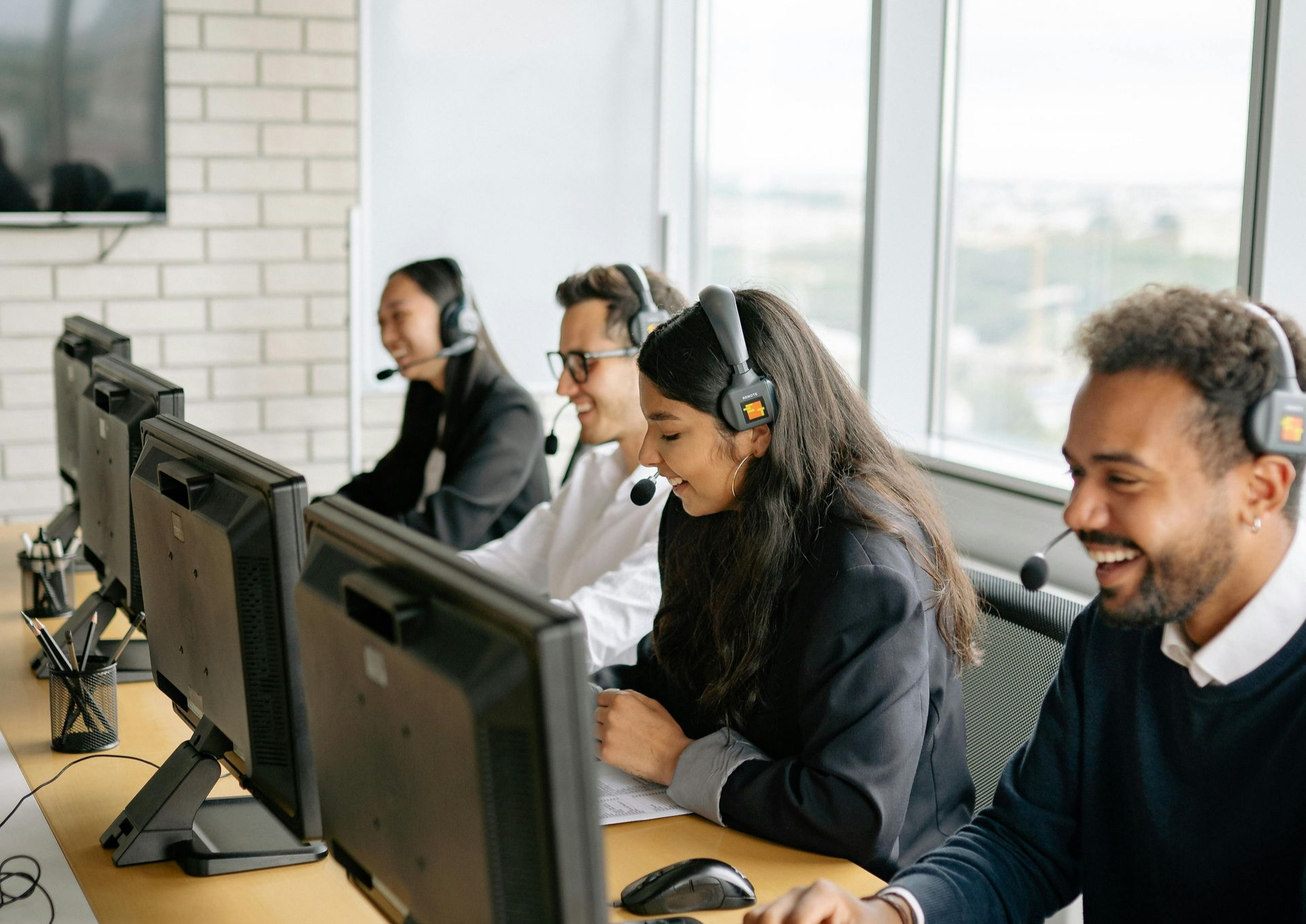 Pessoas usando fones de ouvido, trabalhando em computadores em um ambiente de escritório.