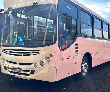 Ônibus cor creme com símbolo de assento acessível, estacionado ao ar livre.