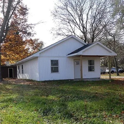 Small white house with a front porch and leafless trees in a grassy yard on a sunny day