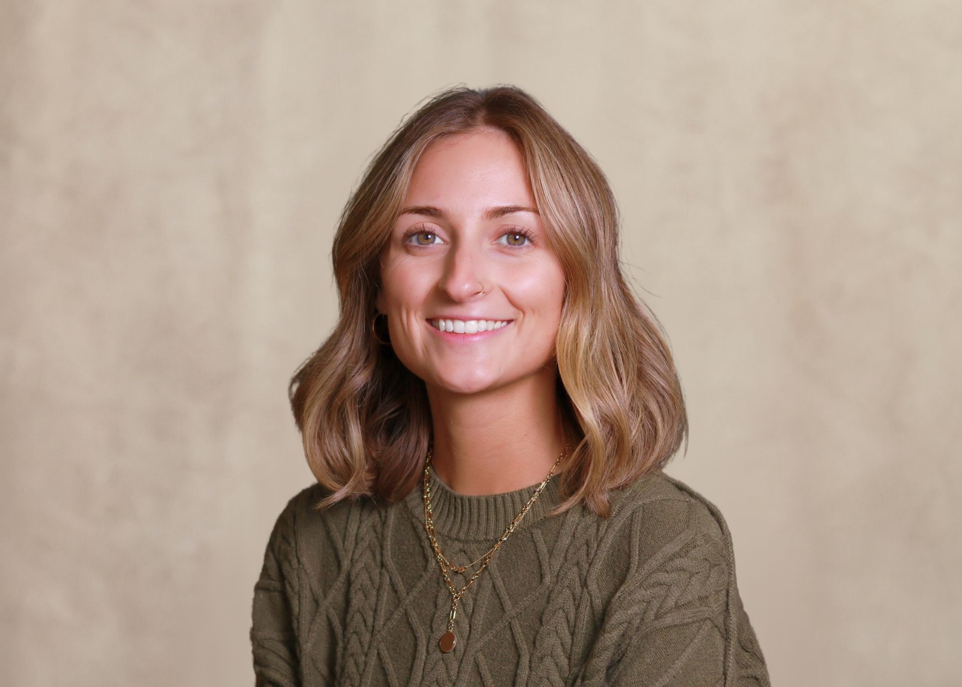 Smiling woman with long wavy blonde hair in a burgundy top against a beige backdrop