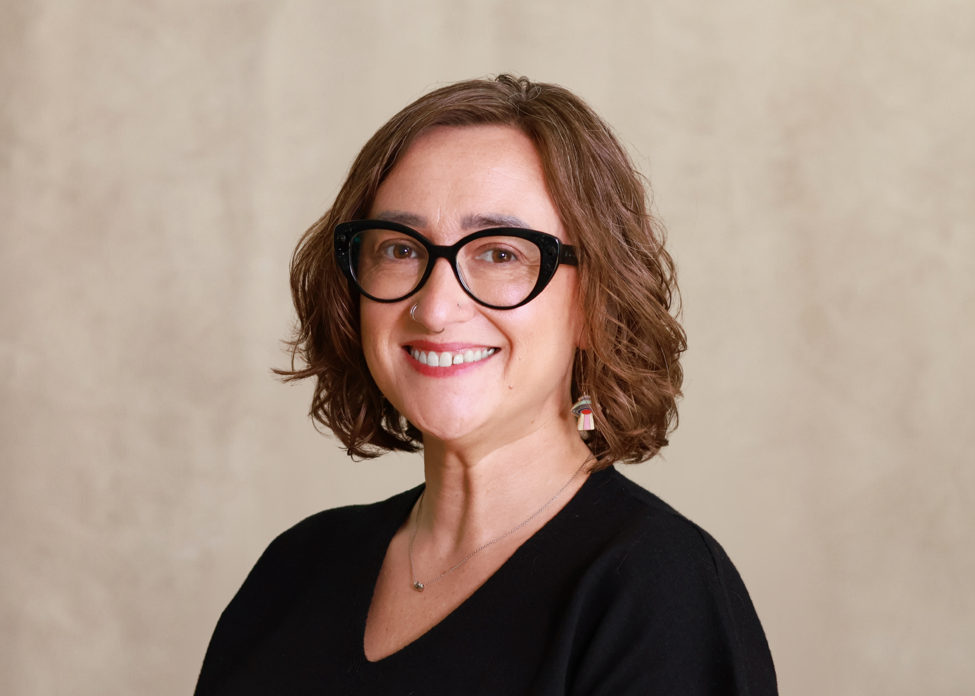 Smiling person with short curly hair and black glasses against a beige background