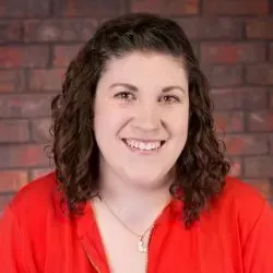 Smiling person in a red top against a brick wall backdrop