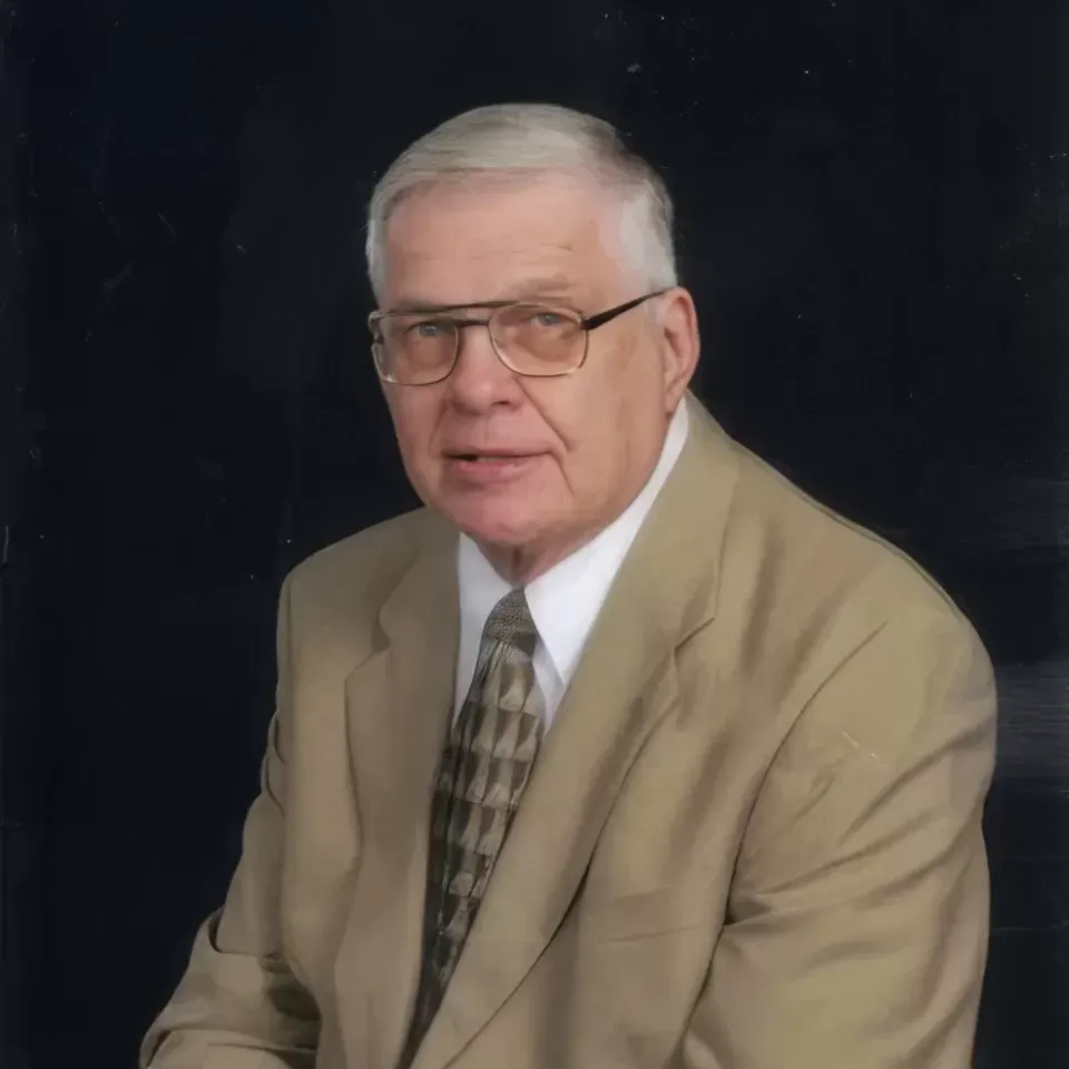Studio portrait of a man in a tan suit and patterned tie against a dark background