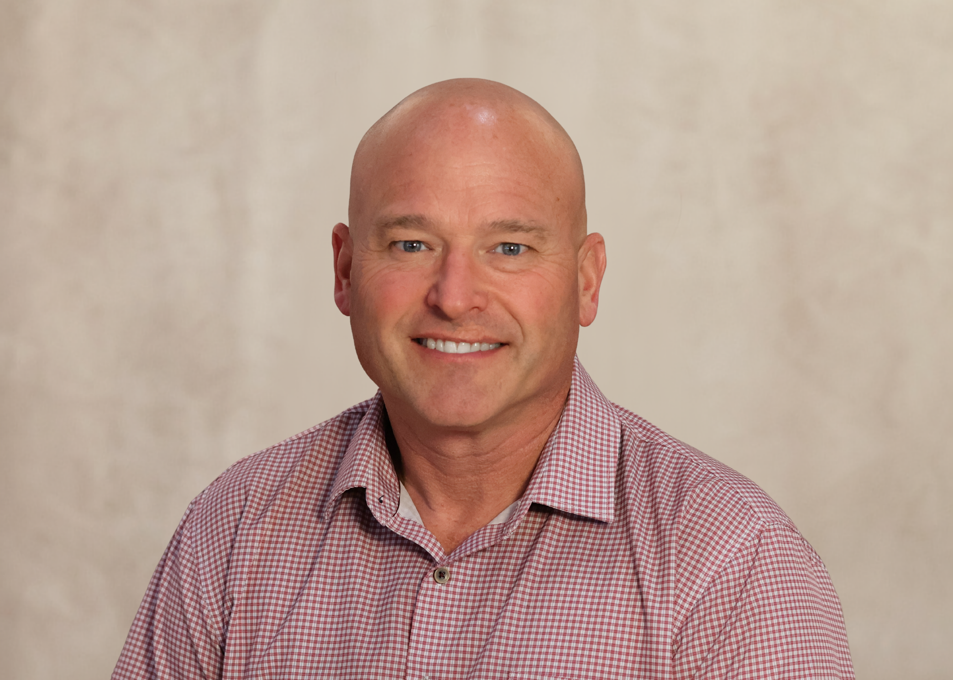 Smiling bald man in a red checkered shirt against a beige studio backdrop