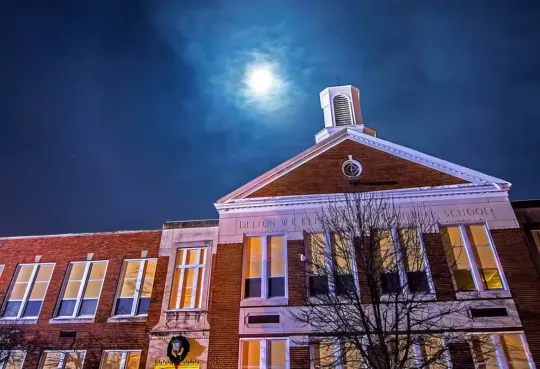 Brick building with a clock tower under a bright moonlit night sky