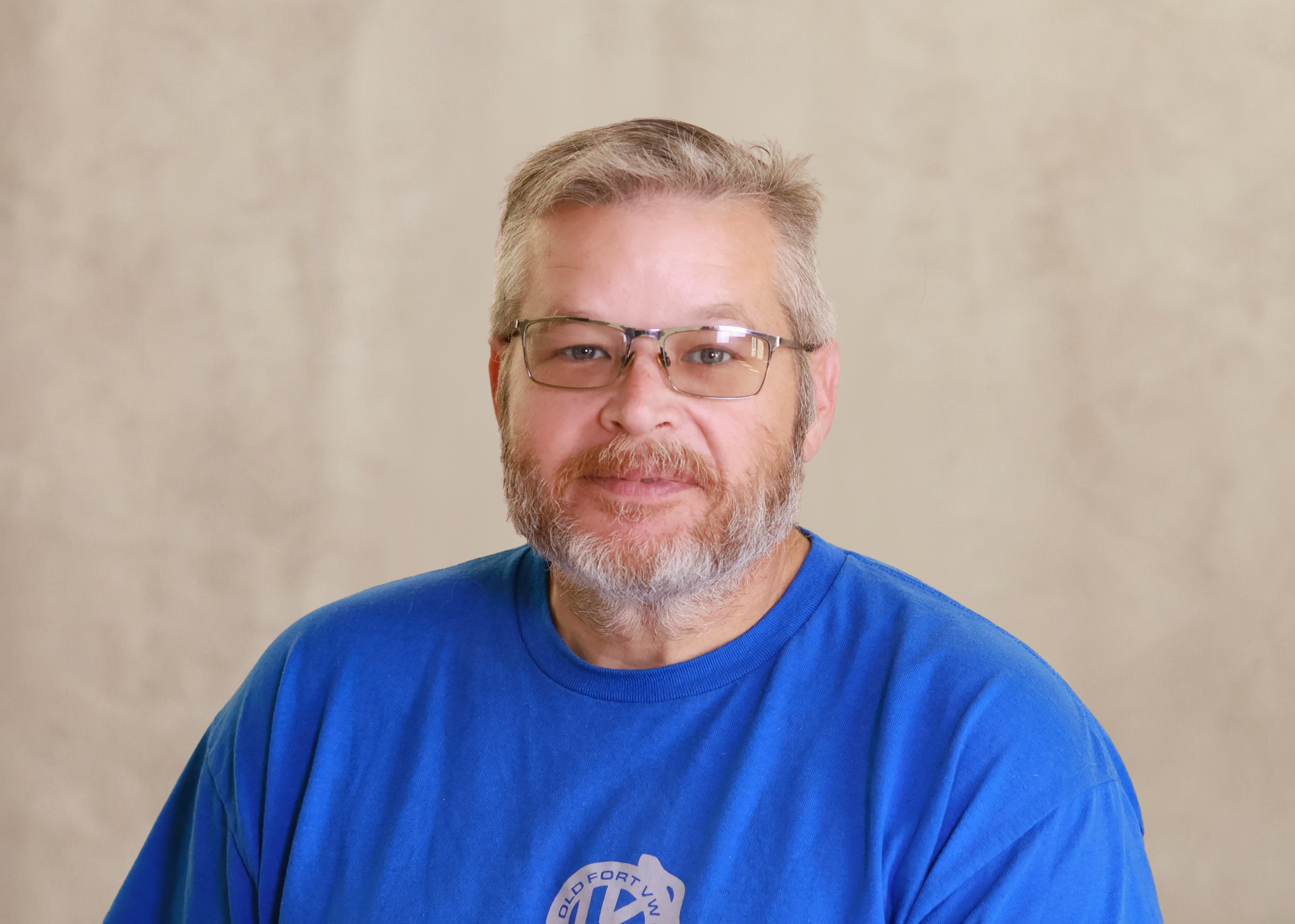 Smiling man with glasses in a blue shirt against a beige background