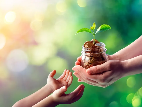 Hands passing a small plant in a glass jar against a soft green, sunlit background