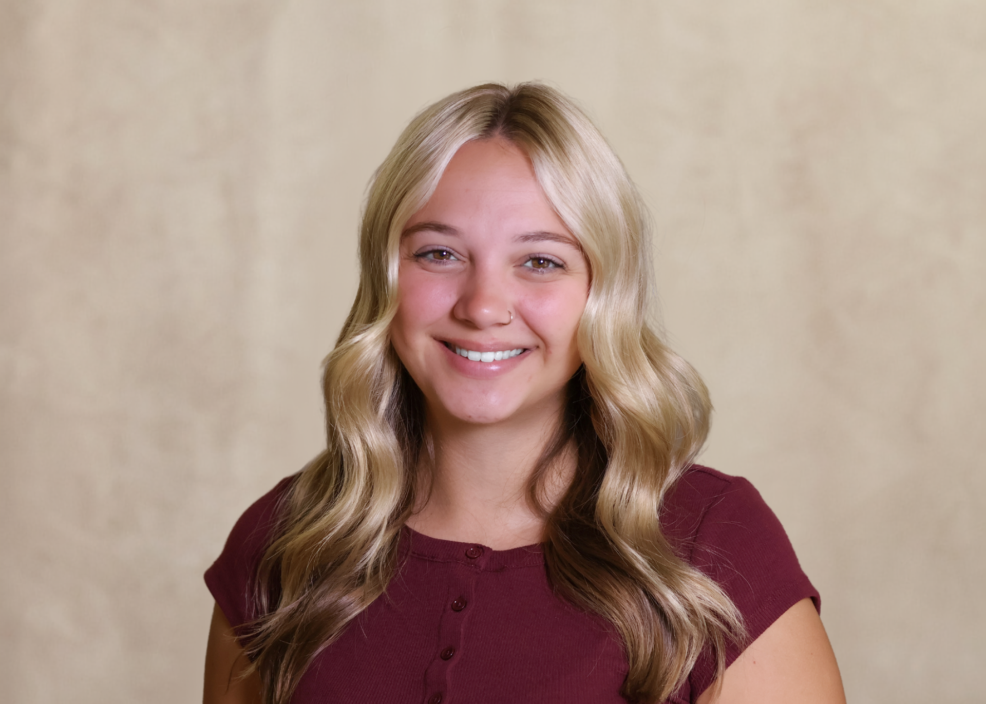 Smiling woman with long wavy blonde hair in a burgundy top against a beige backdrop
