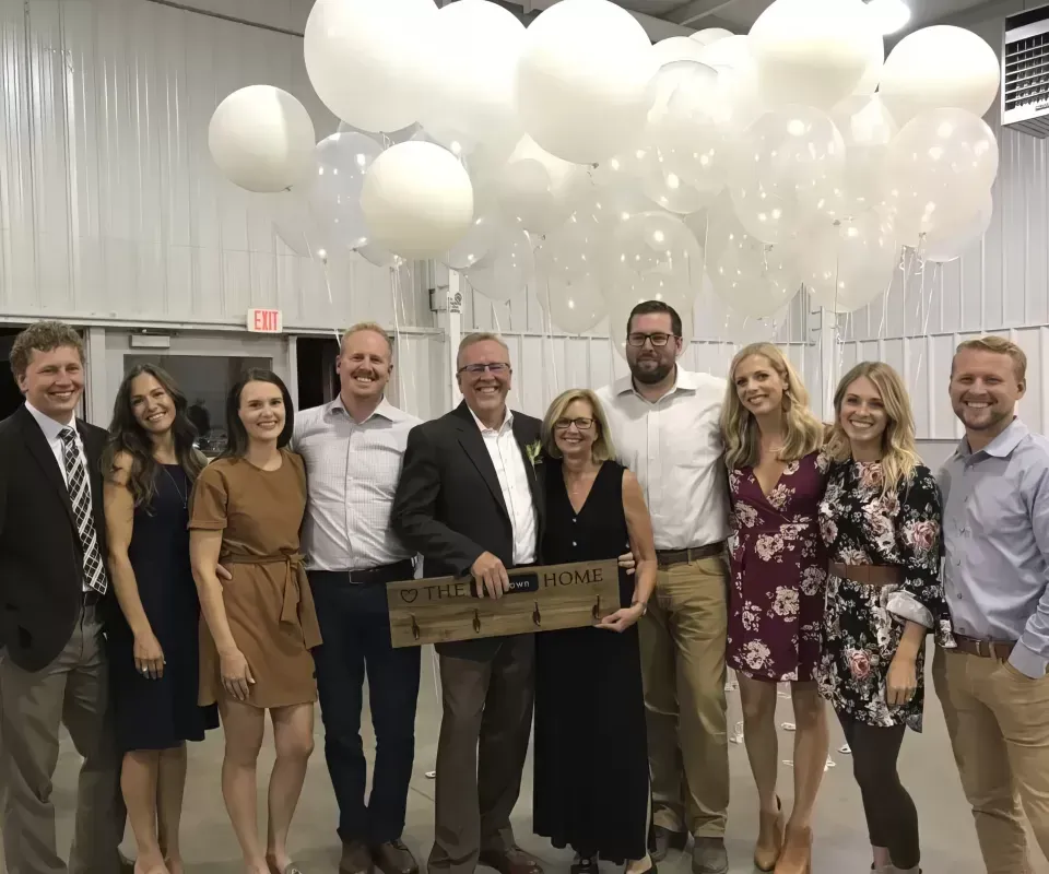 Group of people posing indoors beneath white balloons, holding a large ceremonial key and smiling.