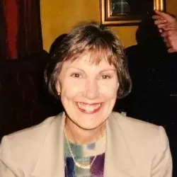 Smiling woman in a beige blazer against a warm indoor background