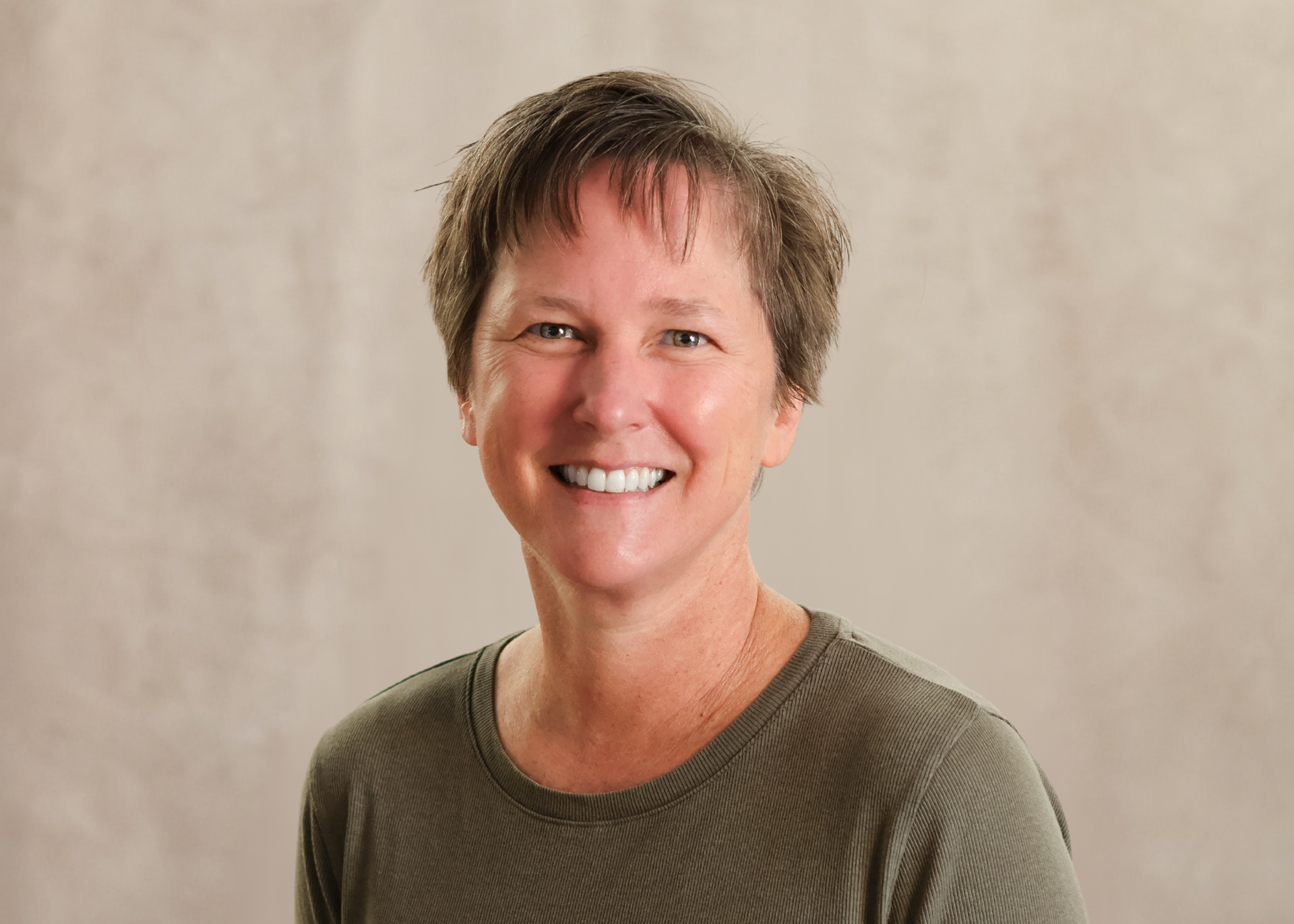 Smiling person in a green sweater against a neutral beige background