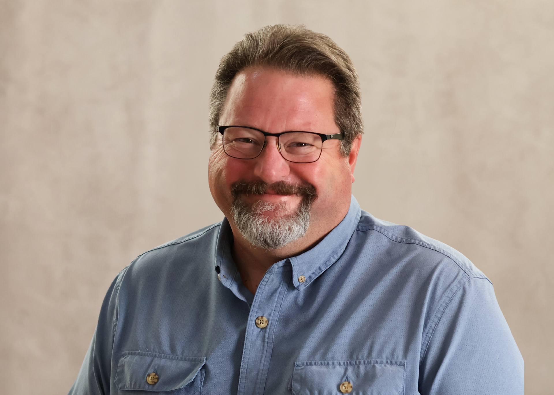 Smiling man in glasses and blue shirt against a neutral background