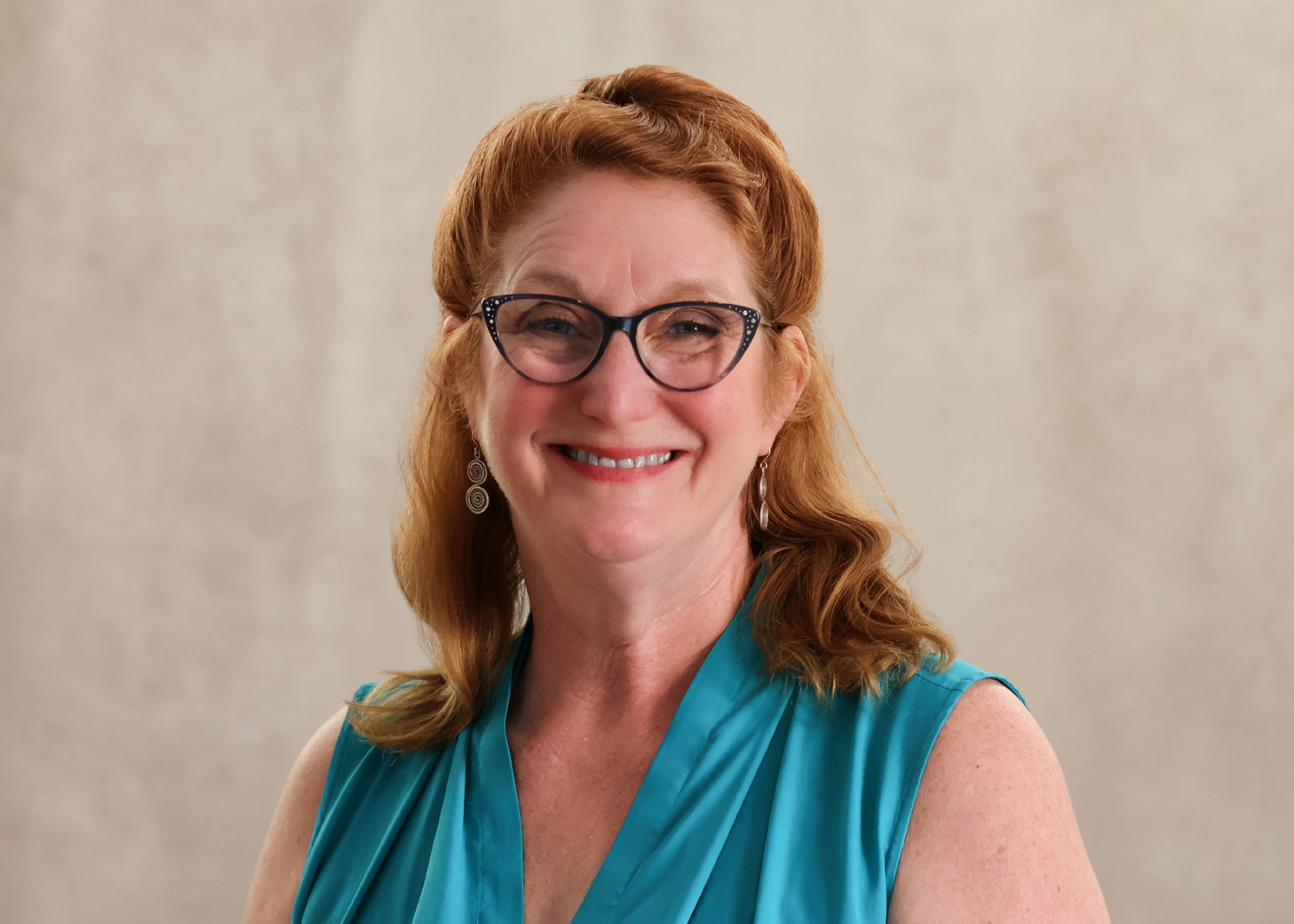Smiling woman in glasses and teal blouse against a plain beige background