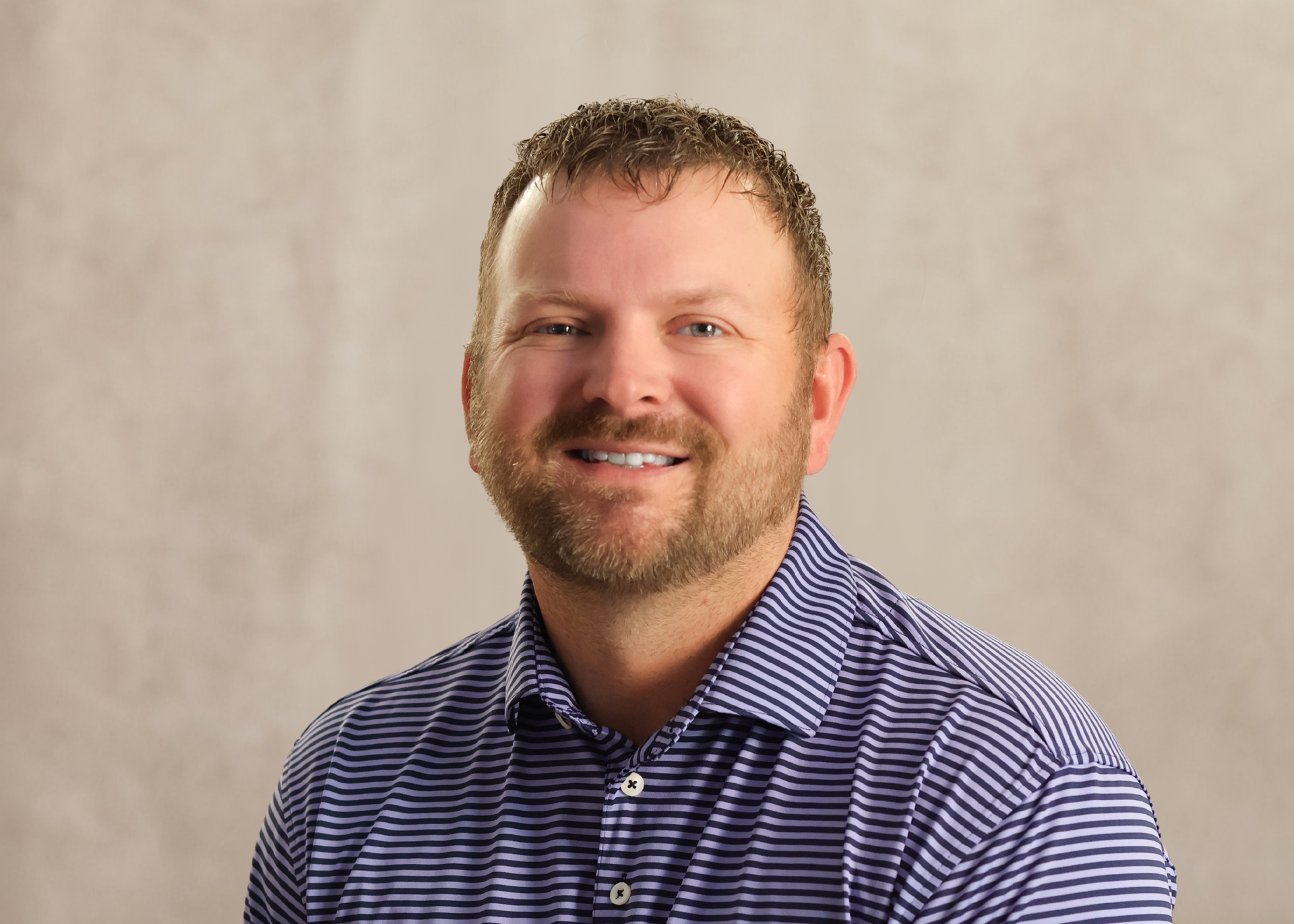 Smiling man in a blue striped shirt against a neutral studio background