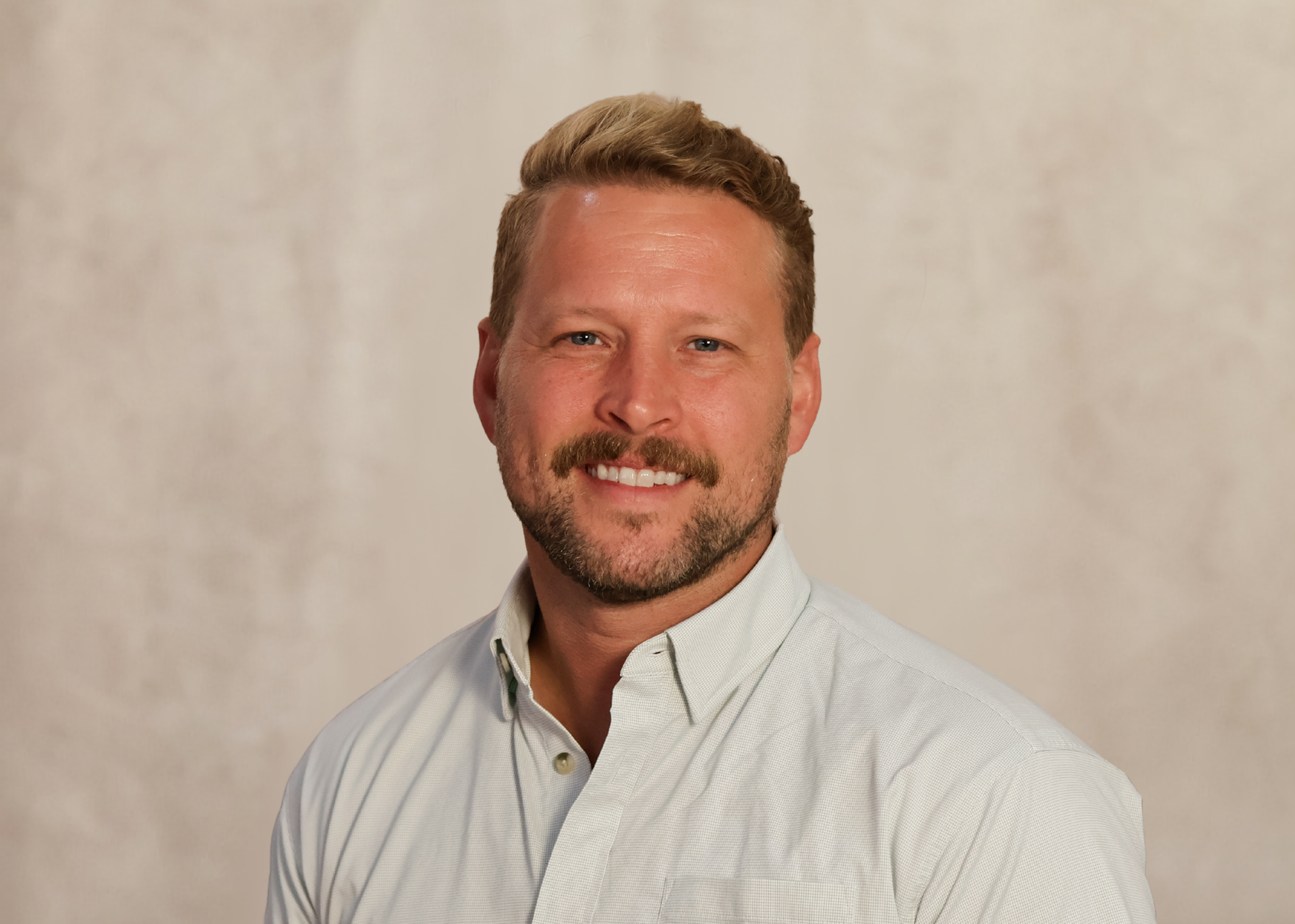 Portrait of a smiling man in a light button-up shirt against a beige backdrop