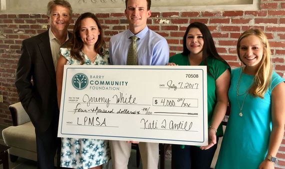 Five people holding a large ceremonial check in front of a brick wall.