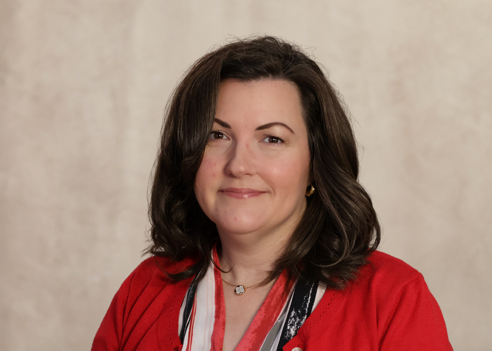 Portrait of a smiling woman in a red jacket against a beige background