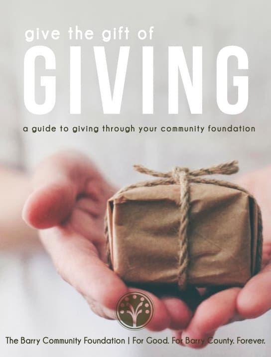 Hand holding a wrapped gift under the words “Give the gift of GIVING” on a community foundation poster