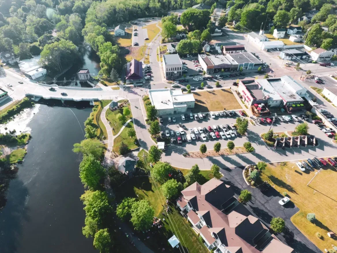 Aerial view of a lakeside park and roadside buildings with parking lots and trees.