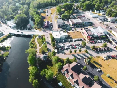 Aerial view of a lakeside park and roadside buildings with parking lots and trees.