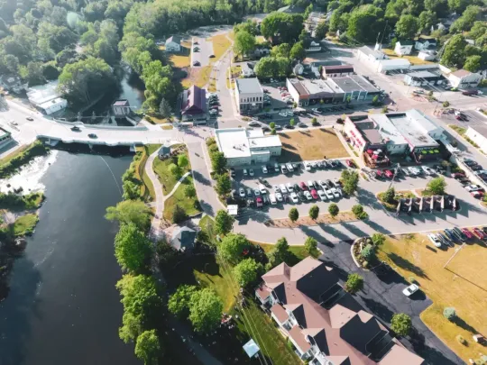 Aerial view of a lakeside park and roadside buildings with parking lots and trees.