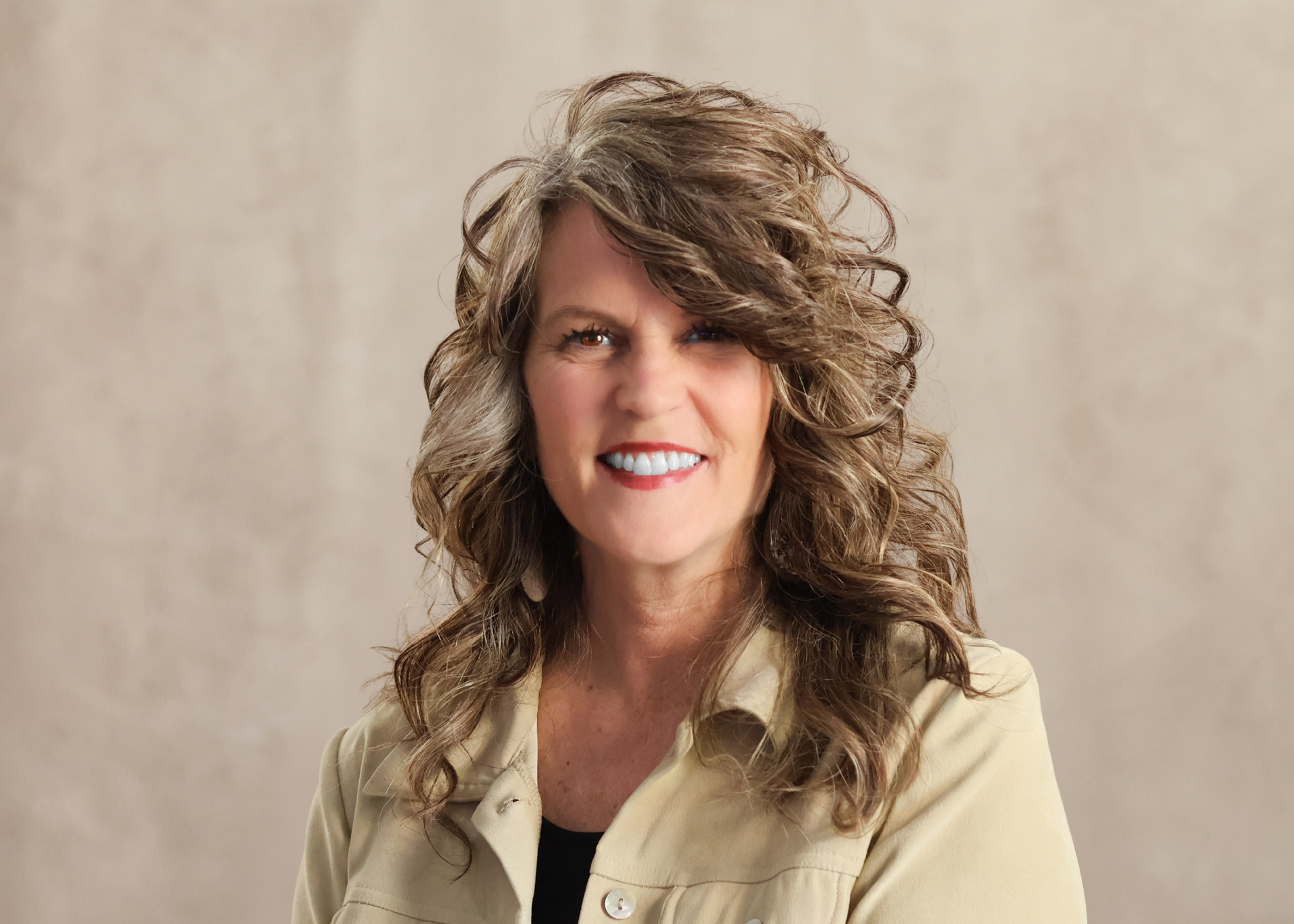 Portrait of a smiling woman with curly hair in a beige jacket against a neutral background