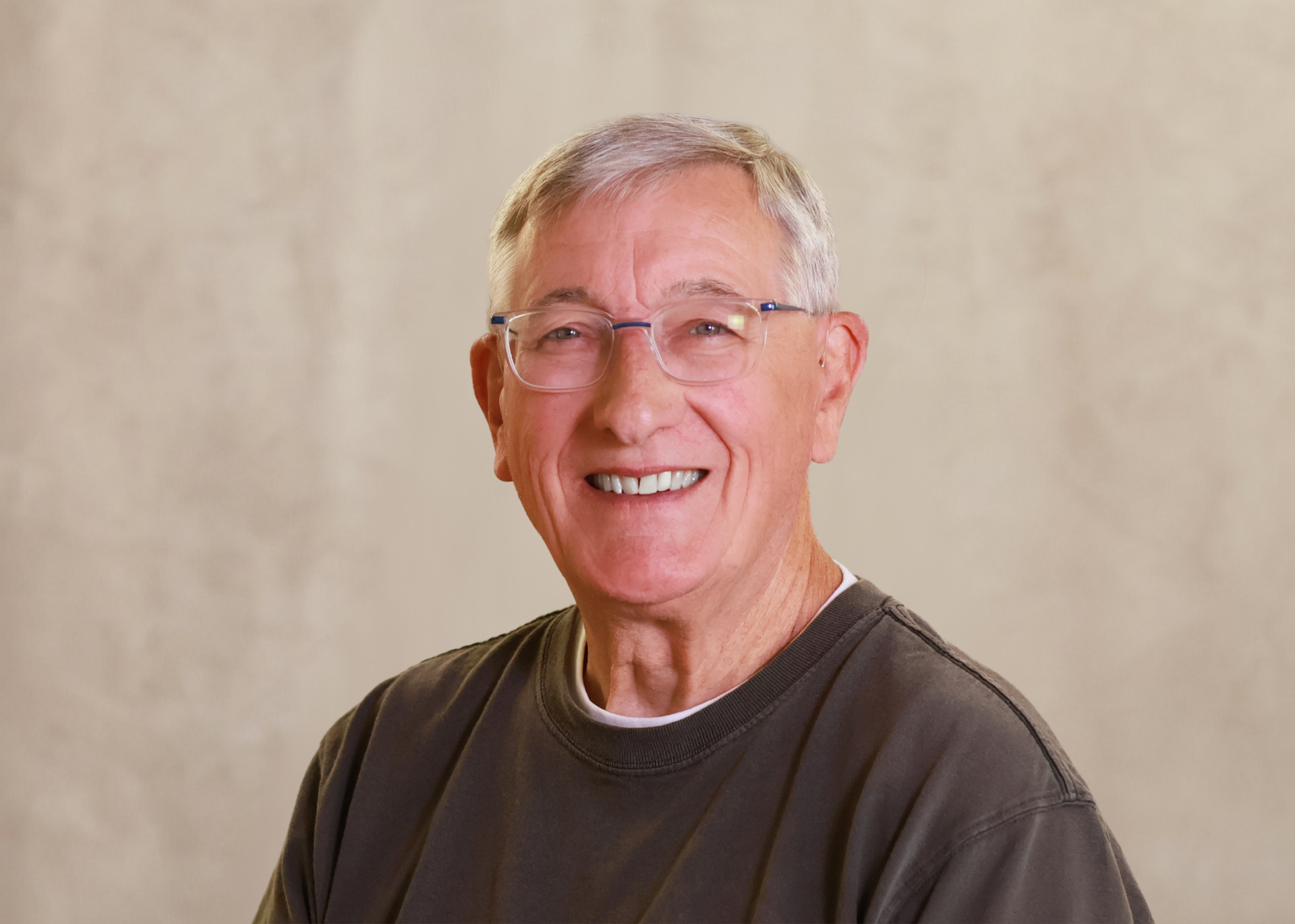 Smiling man with glasses and gray hair in a dark shirt against a beige background