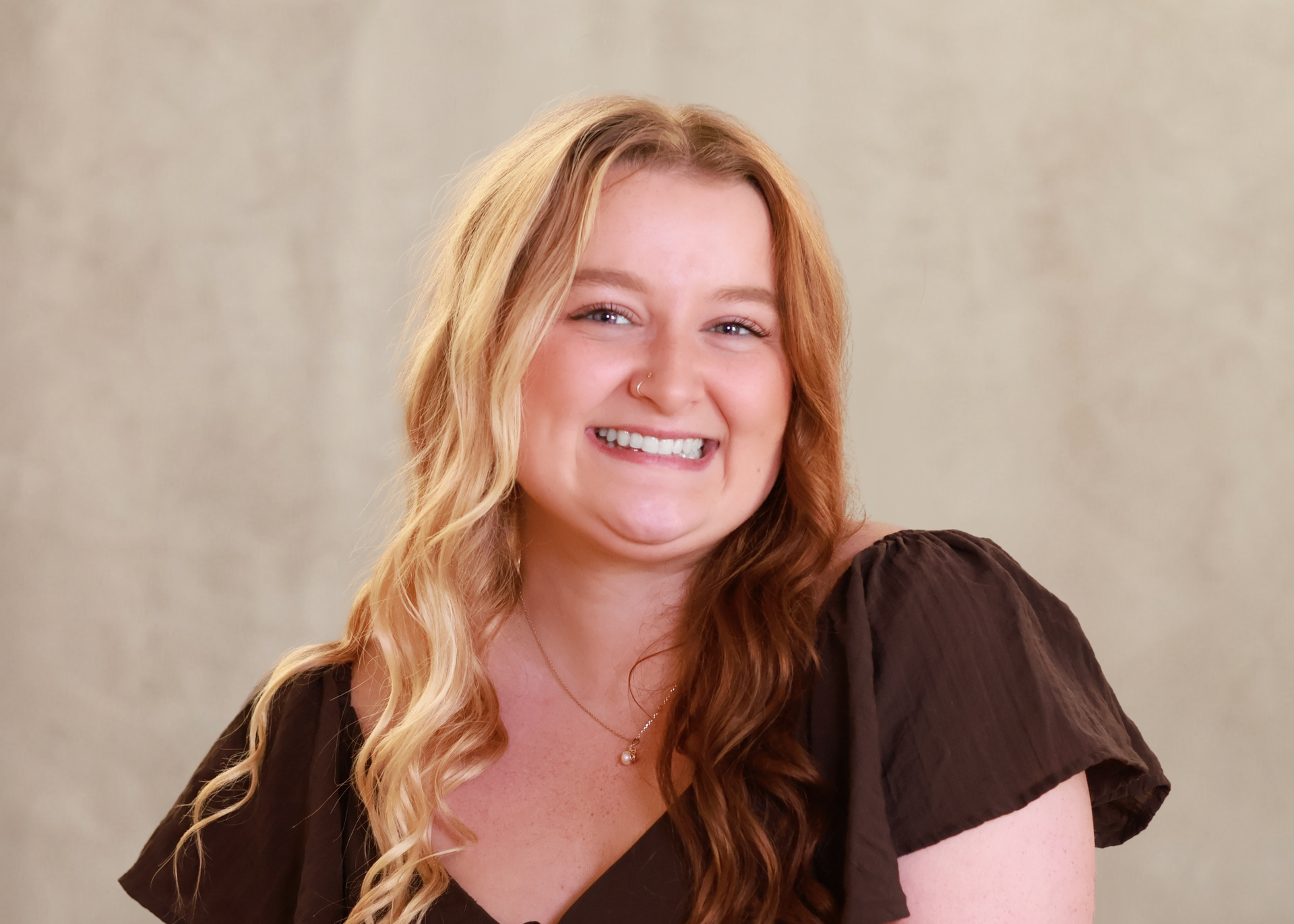 Smiling woman with long blonde hair in a brown dress against a neutral background