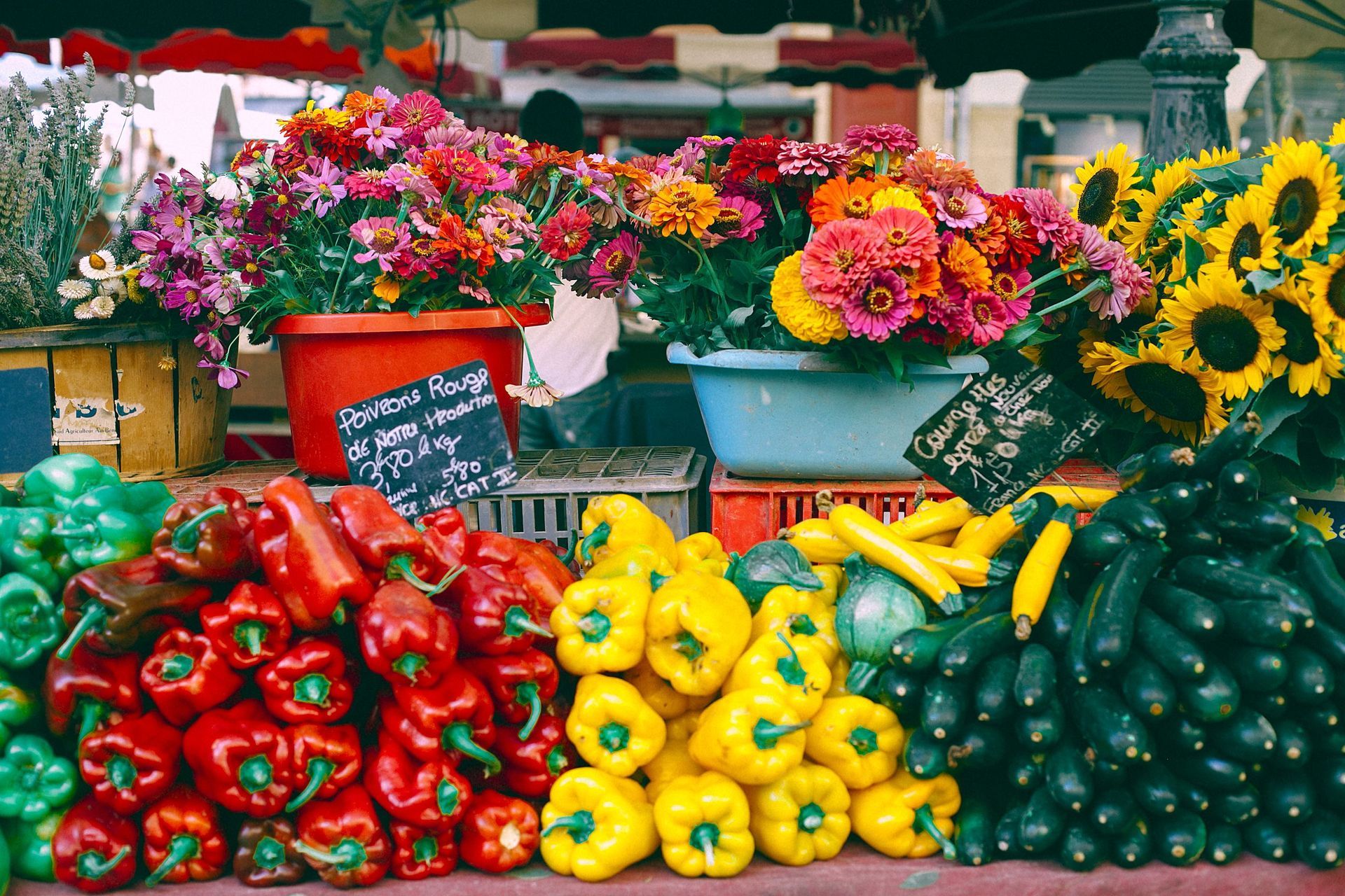 Colorful produce and flower market stall with peppers, squash, and sunflowers