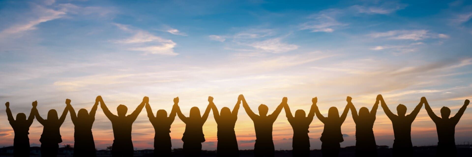Silhouetted people raising arms at sunset on a beach, forming an arch under a pink-orange sky