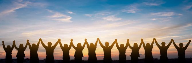 Silhouetted people raising arms at sunset on a beach, forming an arch under a pink-orange sky