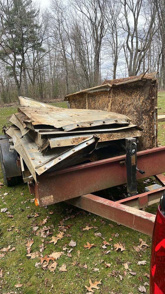 A trailer with a lot of wood on it is parked in the grass.