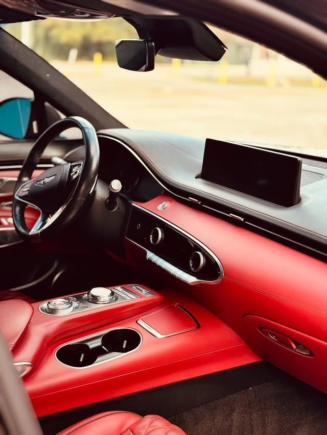 Luxury car interior with red leather seats, black dashboard, and steering wheel near a screen display