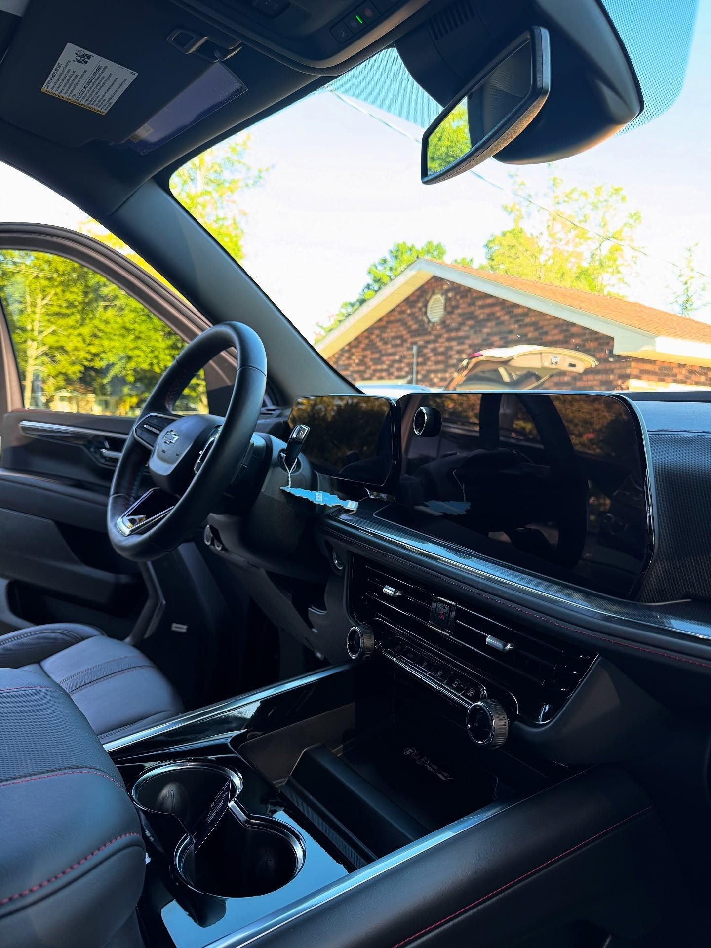 Luxury car interior with black leather seats and dashboard, viewed from the driver’s side with a bright house outside.