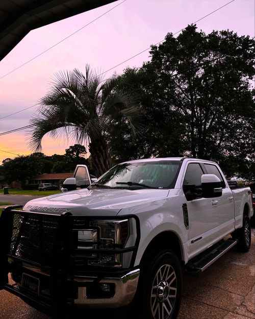 White pickup truck parked on a wet driveway at dusk under pink-purple sky, with trees in the background