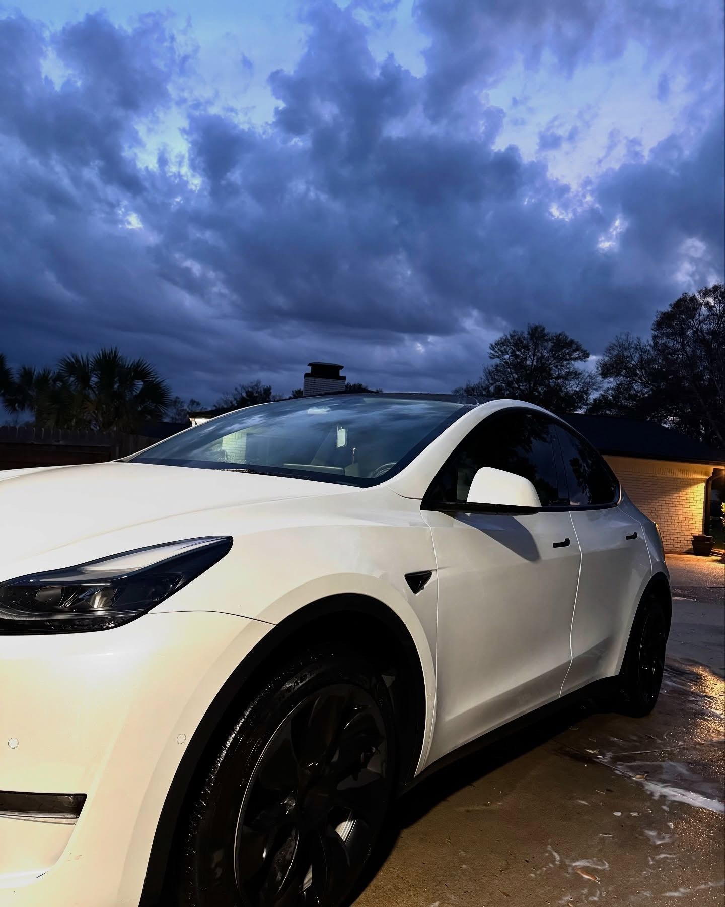 White SUV parked on a wet driveway under a dark cloudy sky at dusk