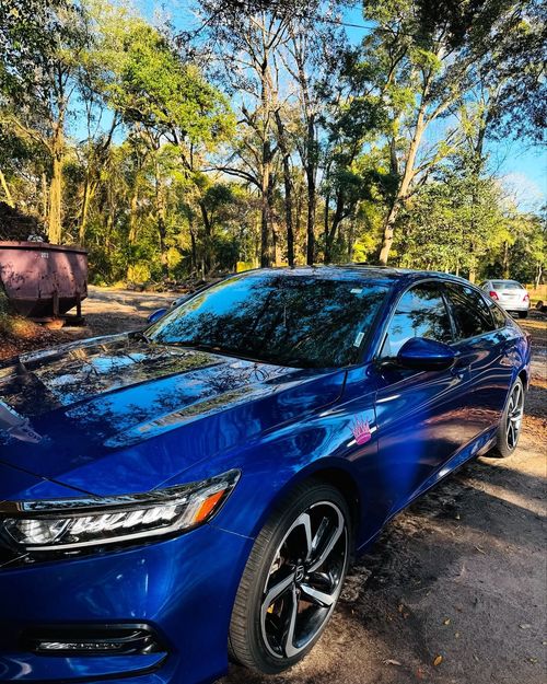 Blue sedan parked on a gravel road in a wooded area on a sunny day