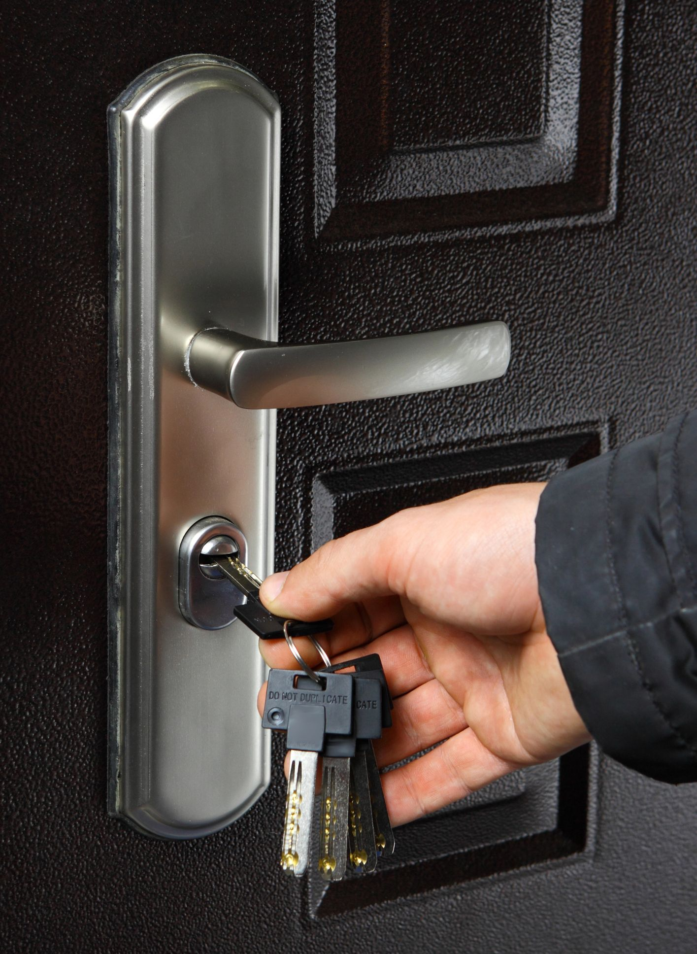 Mano che inserisce la chiave nella maniglia argentata di una porta marrone scuro.