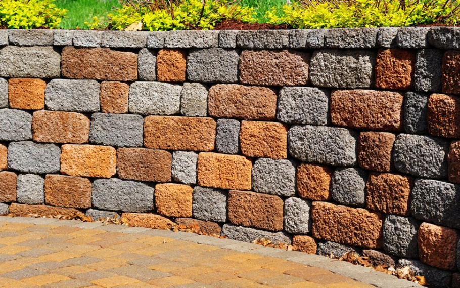 A curved wall made of stacked, textured stones in varied shades of brown, tan, and gray, set against a patio.