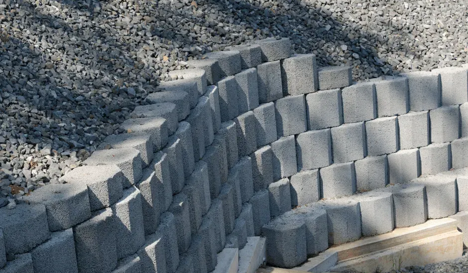 A curved retaining wall made of stacked grey concrete blocks bordering a gravel surface.