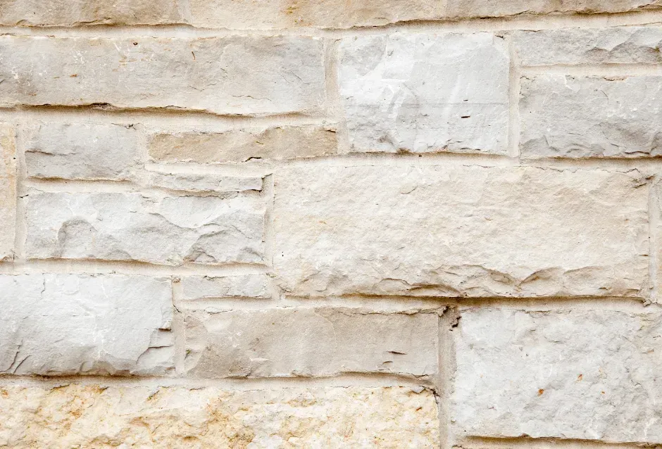 A close-up of a textured stone wall featuring rectangular, light beige and grey blocks of varying sizes.