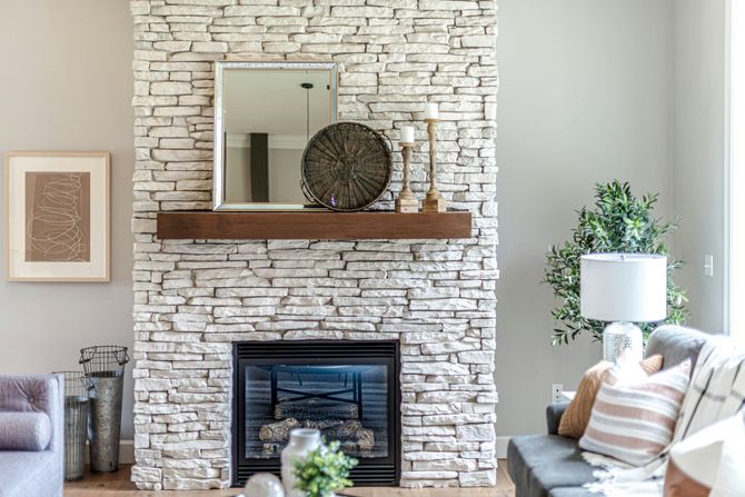 A stone fireplace with a wooden mantel, a mirror, decorative items, and a sofa in a modern living room.