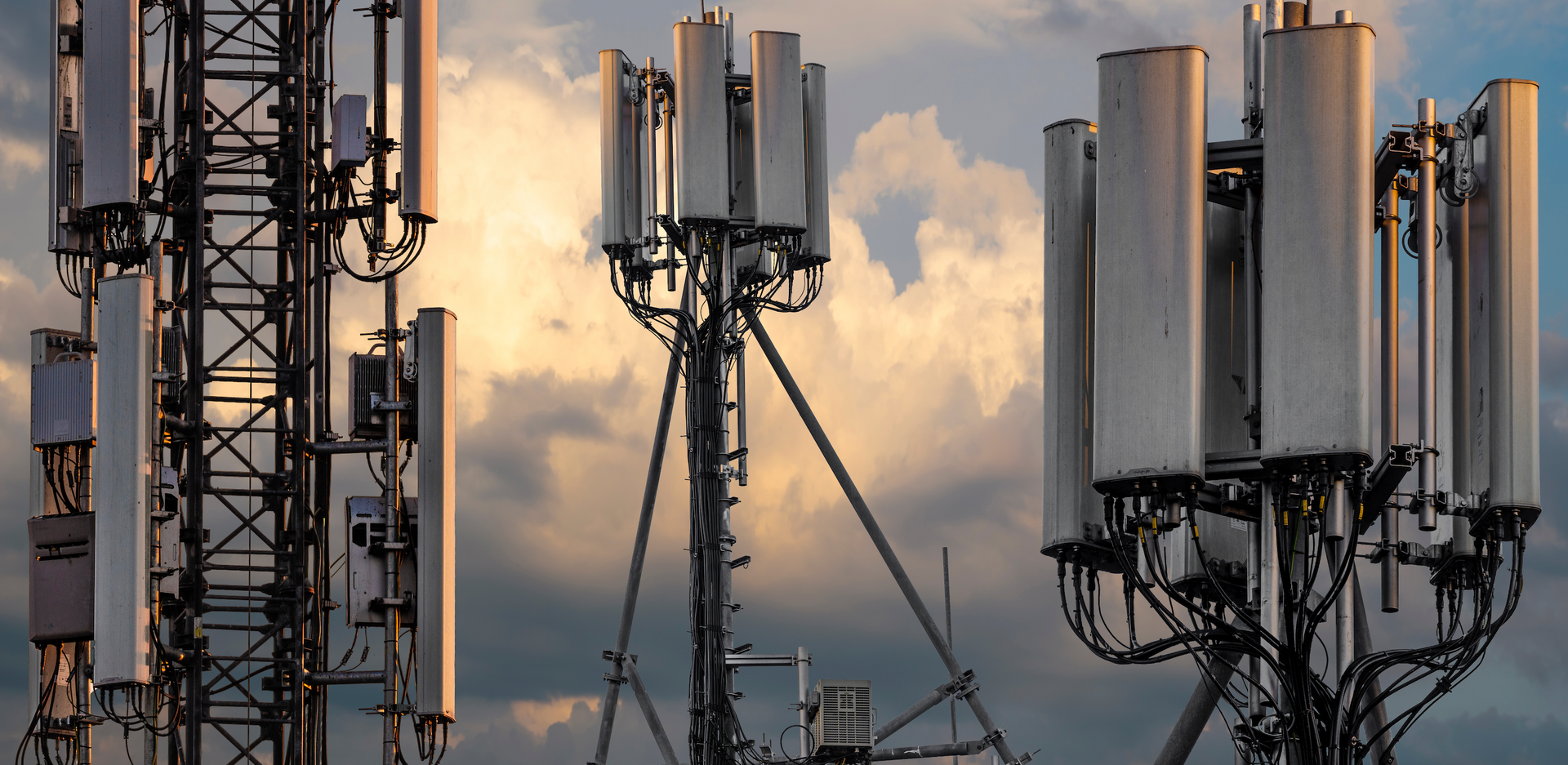 A group of cell phone towers against a cloudy sky.