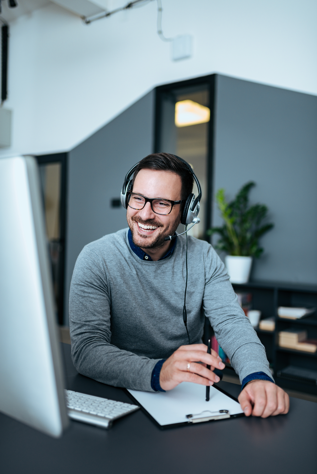 A man wearing headphones is sitting at a desk in front of a computer.