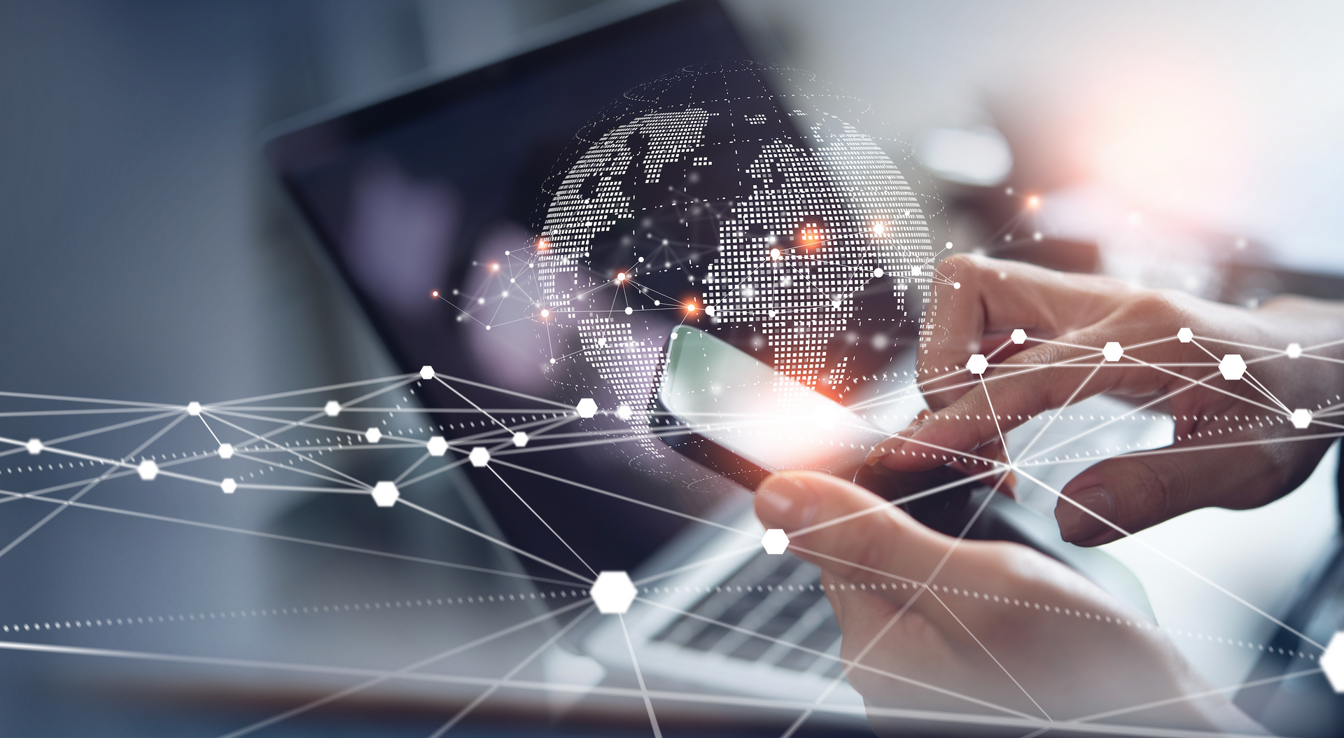 A person is holding a cell phone in front of a laptop computer.