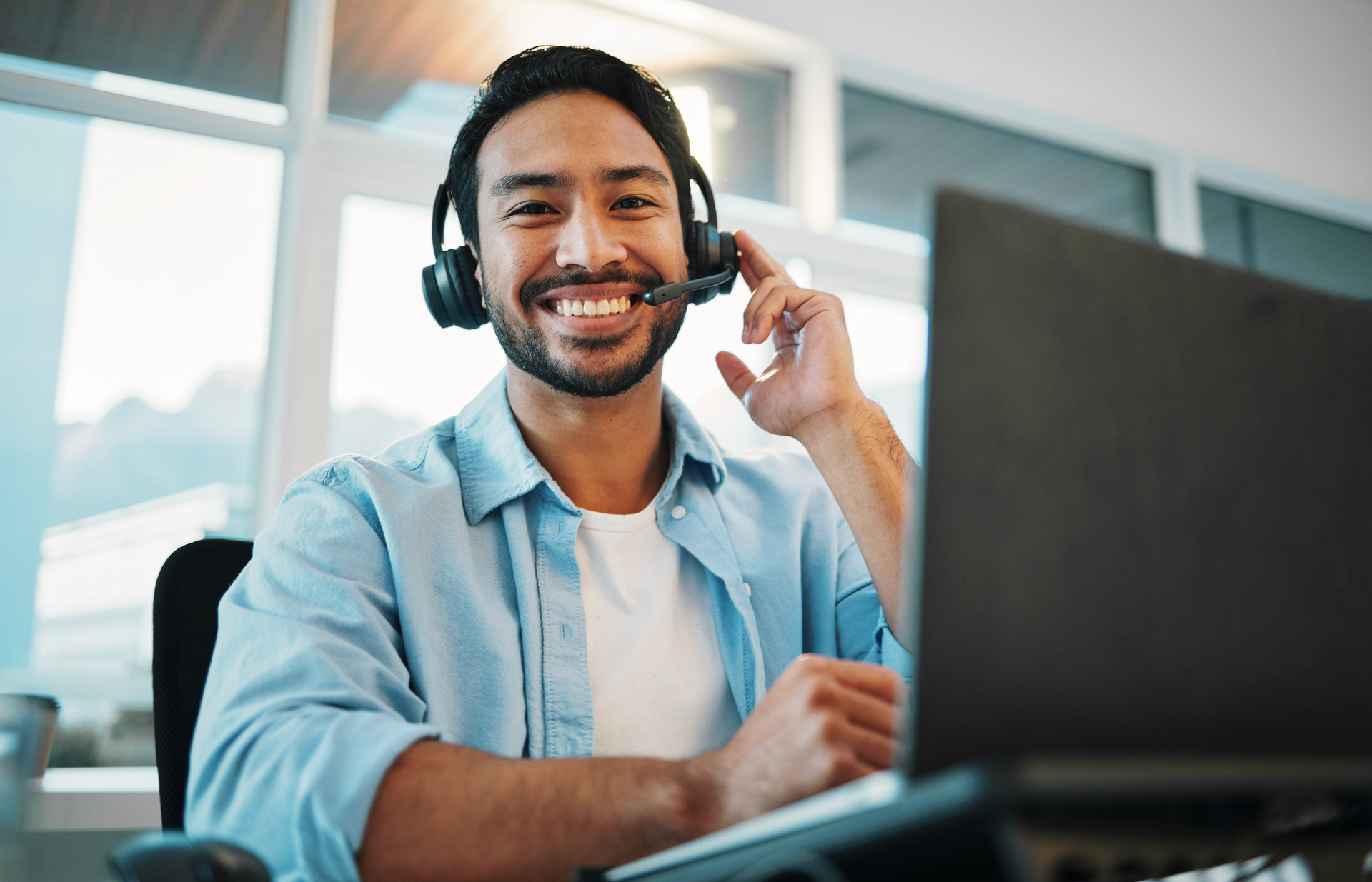 A man wearing a headset is sitting in front of a laptop computer.